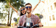 Portrait of happy young couple on scooter enjoying road trip